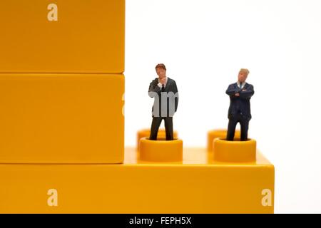 Miniatur Figur Business-Männer in Anzügen stehen auf gelb Kunststoff bauen von Backsteinen Stockfoto