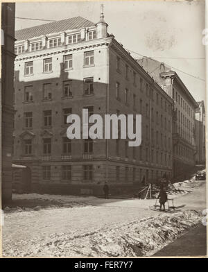 Das Foto zeigt eine Winterszene auf einer Straße in Helsinki, Finnland, die historische architektonische Strukturen vor verschneiten Kulissen zeigt. Das kalte Klima spiegelt sich in Kleidung und Atmosphäre wider. Stockfoto