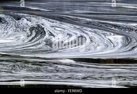 Abstrakte weißen geschwungenen Schaum wirbelt Muster auf dunklen Teich Wasser. Stockfoto