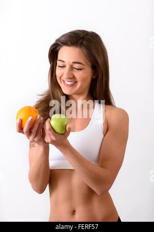Junge schlanke Frau im Sport Top entscheiden zwischen Orange und Apfel Stockfoto