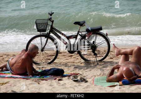 Ein Fahrrad mit einem Sozius Beifahrersitz mit zwei ältere Männer, Sonnenbaden und relaxen am Strand in Pattaya Thailand geparkt. Stockfoto