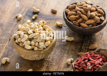 Cashew-Kerne, getrocknete Goji-Beeren und Mandeln in der Schale auf strukturierten hölzernen Hintergrund. Selektiven Fokus Stockfoto