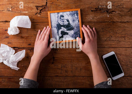 Nicht erkennbare traurige Frau hält gebrochene Bild des Paares in der Liebe. Stockfoto