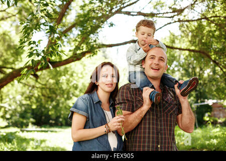 Glückliche Familie im Freien zu Fuß. Schwangere Frau, Mann und kleiner Junge sitzt auf Vater. Spaß zu haben. Familienwerte Konzept. Natürliche Stockfoto