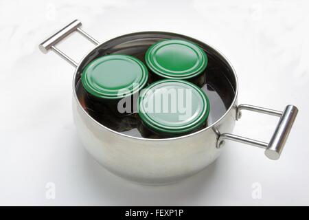 Stahltopf mit drei Gläsern im Wasser kochen. Isoliert auf weißem Hintergrund Stockfoto