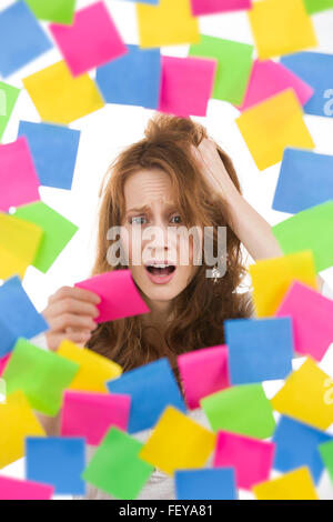Betonte Frau mit rosa Note umgeben von bunten Papieren Stockfoto