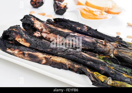 Nahaufnahme einer Platte mit einigen gegrillte Calcots, süße Zwiebeln und eine Schüssel mit Romesco-Sauce, typisch für Katalonien, Spanien, auf einem Satz Stockfoto