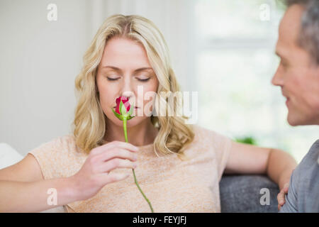 Hübsche Frau eine Rose riechen angeboten von Ehemann Stockfoto