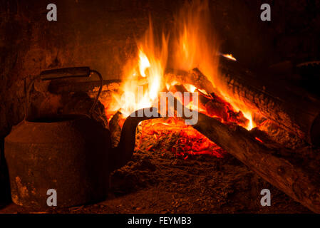 Am alten gemauerten Kamin mit brennendem Holz und Wasserkocher. Winterzeit warm drinnen Szene. Stockfoto