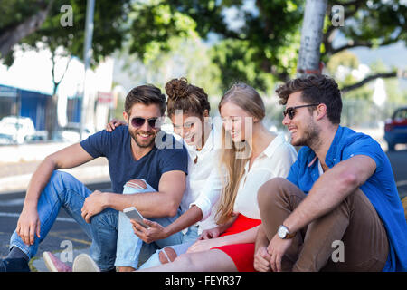 Hip Freunde Blick auf Smartphone und sitzen auf Bürgersteig Stockfoto