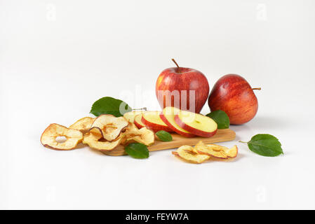 frische rote Äpfel und Apfelringe auf Holzbrett Stockfoto