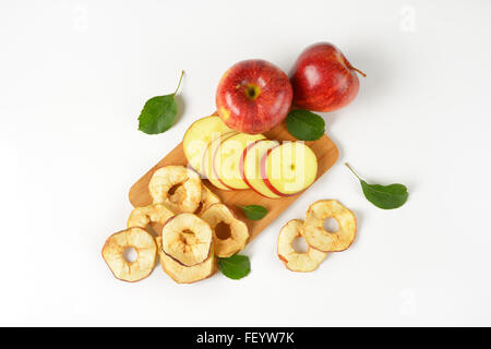 frische rote Äpfel und Apfelringe auf Holzbrett Stockfoto