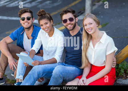 Hip Freunde Tablet halten und sitzen auf dem Bürgersteig Stockfoto