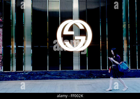 Asiatische Frau mit Handtasche auf Handy zu Fuß durch beleuchtet Gucci Logo im Zentrum von Hongkong Store Stockfoto