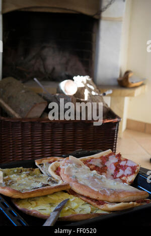 Scheiben von hausgemachten Pizza serviert auf einem Holztisch Aroun einen Kamin Stockfoto