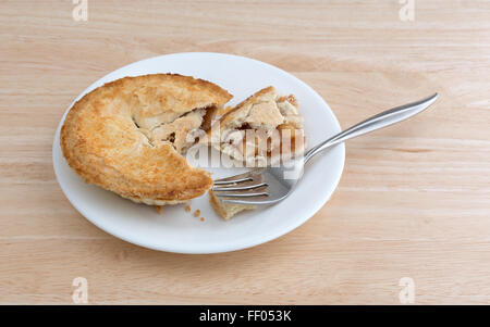 Eine kleine Apfelkuchen auf einem Teller mit der Gabel oben auf einer hölzernen Tischplatte mit natürlichem Licht beleuchtet. Stockfoto