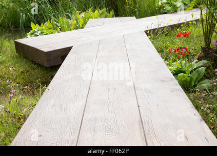 Ein Wildtiergarten mit Holzsteg Brett Gehweg über einen kleinen Bach Wasser Feature UK Stockfoto