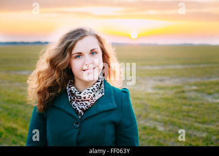 Porträt der schönen Plus Size junge Frau im blauen Mantel posiert In Feld Wiese am Sonnenuntergang Hintergrund. Frühling, Outdoor Portrait Stockfoto