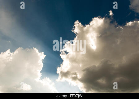 Die Sonne scheint hinter einer Schicht aus Cumulus-Wolken, die Lichtstrahlen durch den Himmel werfen. Dieser atmosphärische Effekt erzeugt eine dramatische und malerische Szene. Stockfoto