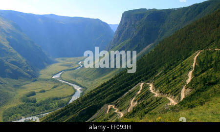 Ein Bach fließt durch ein steiles Tal und bietet einen malerischen Blick auf die Natur. Das klare Wasser fließt über Felsen, umgeben von Hängen und einem üppig grünen Pfad. Stockfoto