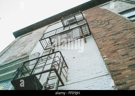 Eine Feuertreppe an einem städtischen Gebäude. Die Backsteinstruktur steht im Kontrast zu Graffiti-Kunstwerken, während die Metallleiter den Zugang zu den höheren Stockwerken des Gebäudes ermöglicht. Stockfoto
