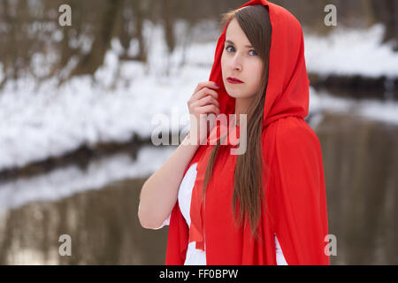 Ein Mädchen im roten Umhang steht nahe dem Fluss im winter Stockfoto