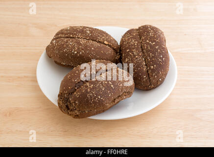 Drei Brötchen frisch Mehrkorn auf einem weißen Teller oben auf einer hölzernen Tischplatte mit natürlichem Licht beleuchtet. Stockfoto