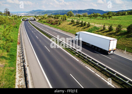 Korridor-Autobahn mit den Übergang für die Tierwelt, geht die Autobahn weißen LKW, im Hintergrund die Stadt Stockfoto