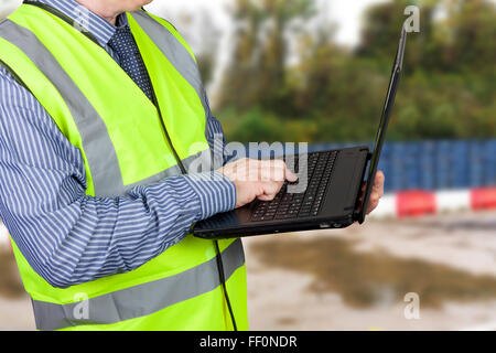 Bau Gutachter in Hallo Vis-Weste, die Eingabe von Daten in seinen Laptop auf seiner Baustelle Stockfoto