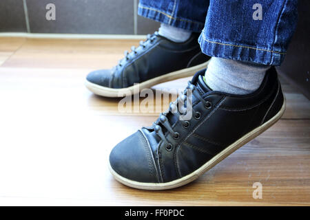 Des Kindes Bein in Blue Jeans und schwarze Schuhe auf Holzboden Stockfoto