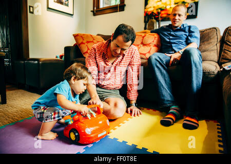 Schwule Väter spielen mit Baby Sohn im Wohnzimmer Stockfoto