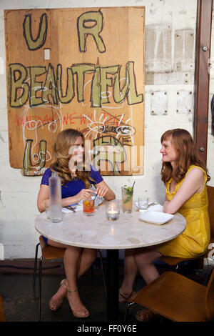 Zwei Frauen, die gemeinsame Mahlzeit im Restaurant Mua in Oakland, Kalifornien, liest das Kunstwerk hing an der Wand hinter ihnen U R schön. Stockfoto