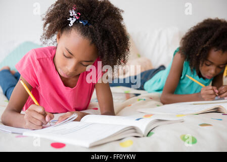 Gemischte Rassen Schwestern Hausaufgaben auf Bett Stockfoto