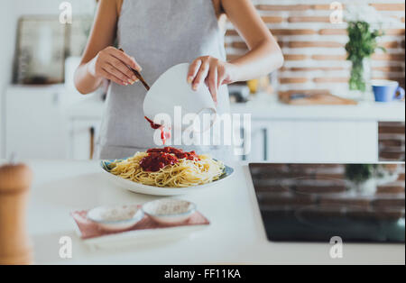 Kaukasische Frau Gießen Soße auf Nudeln in Küche Stockfoto