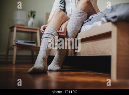 Kaukasische Frau sitzt am Bett hochziehen Socken Stockfoto