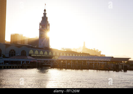 San Francisco Ferry Building am Embarcadero mit der untergehenden Sonne scheint hinter der Uhrturm aus dem Wasser fotografiert. Stockfoto