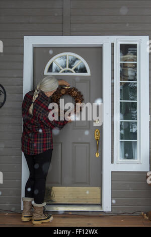 Ältere Frau kaukasischen Kranz an Eingangstür hängen Stockfoto