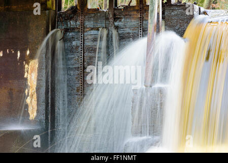 Wasser über den Rand eines kleinen Damms Kaskadierung. Wasser ist bräunlich und Mineralien reich. Dam hat kleine Löcher auf der Seite, die auslaufen. Stockfoto