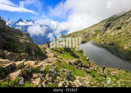 Niedrige Wolken und Nebel um Grandes Jorasses und Mont-Blanc, während Wanderer am Lac De Cheserys, Haute Savoie, französischen Alpen gehen Stockfoto