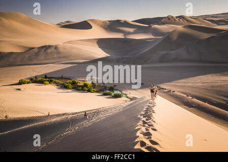 Touristen-cRMimbing-Sand-Dünen bei Sonnenuntergang in Huacachina, einer ViRMRMage in der Wüste, Ica Region, Peru, Südamerika Stockfoto