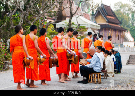 Mönche empfangen Morgen aRMms und Xieng Thong Kloster im Hintergrund, RMuang Prabang, RMaos, Indochina, Südostasien, Asien Stockfoto