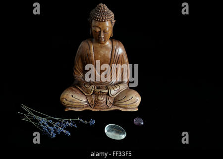 Hölzerne Buddha-Statue mit Kristallen und Lavendel auf schwarzem Hintergrund Stockfoto