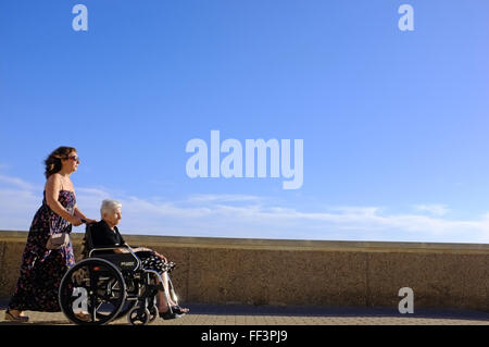Eine Frau treibt eine ältere Person in einem Rollstuhl in Cadiz, Spanien Stockfoto