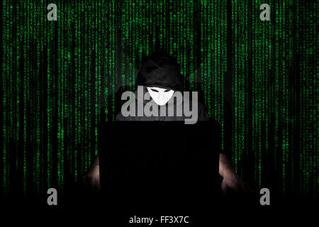 Ein maskierter Mann auf einen Laptop als Symbol für die Gefahren des Internets. Stockfoto