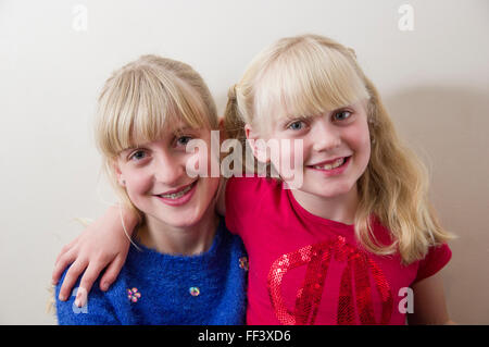 Studio-Porträt von zwei jungen, blonden Mädchen mit ihre Arme umeinander vor einem weißen Hintergrund. Stockfoto