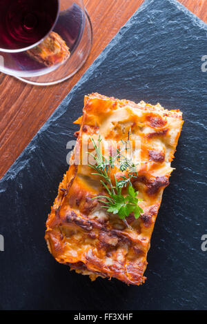 heiß dampfende Lasagne mit Rotwein auf Schiefer und Holz Tisch Stockfoto