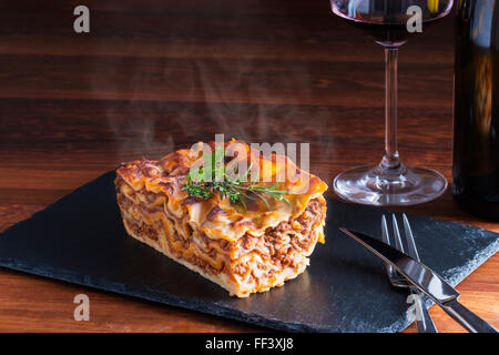 heiß dampfende Lasagne mit Rotwein auf Schiefer und Holz Tisch Stockfoto