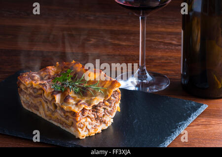 heiß dampfende Lasagne mit Rotwein auf Schiefer und Holz Tisch Stockfoto