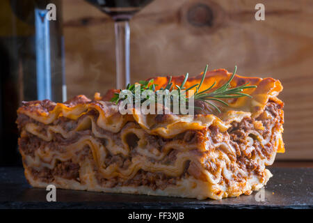 heiß dampfende Lasagne mit Rotwein auf Schiefer und Holz Tisch Stockfoto