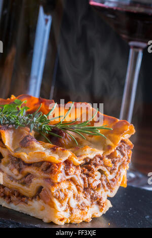 heiß dampfende Lasagne mit Rotwein auf Schiefer und Holz Tisch Stockfoto